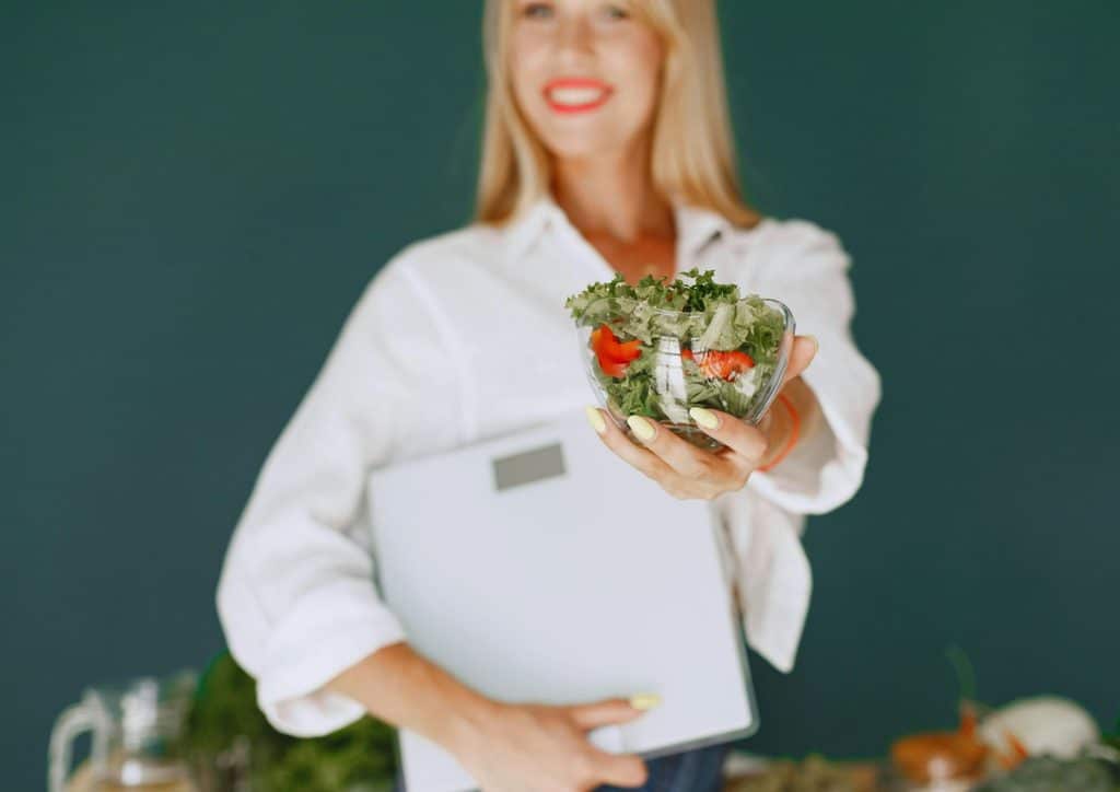 Clinical Nutritionist vs Nutritionist: What's the Difference 7 A woman smiling while holding a colourful salad in her hand, showcasing fresh vegetables and greens.