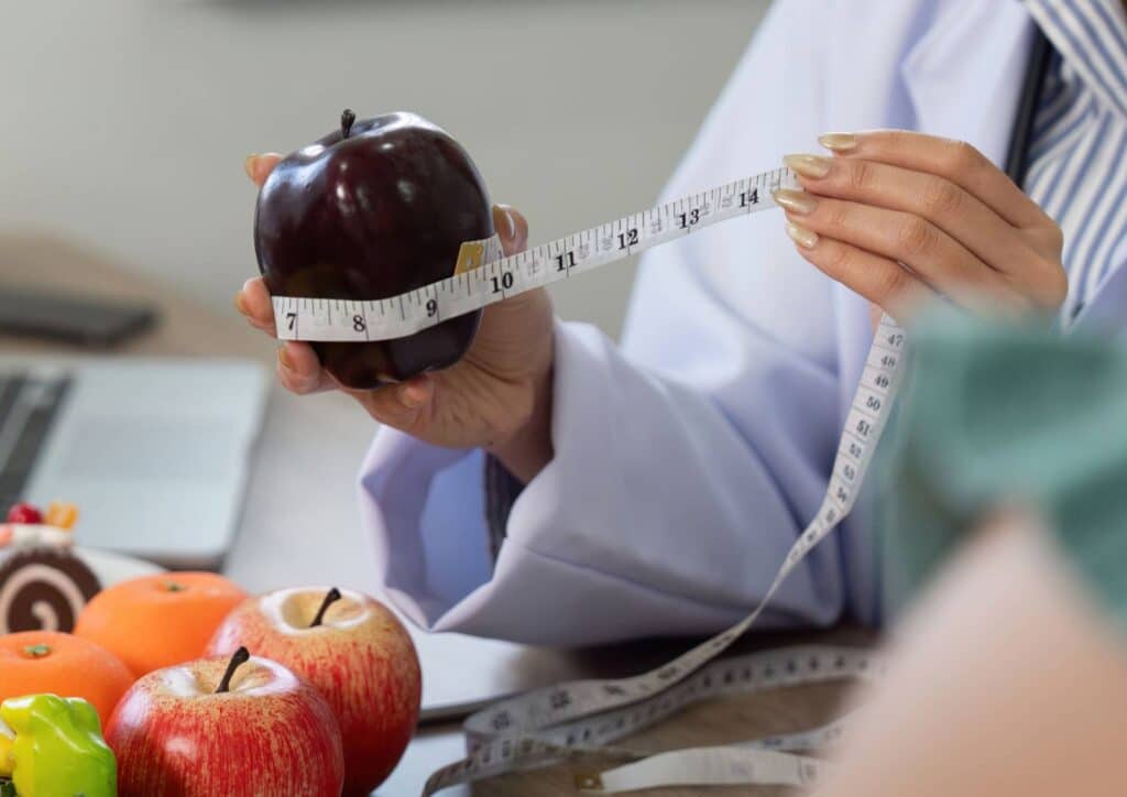 Nutritionist vs Clinical Nutritionist: What's the Difference? 6 A doctor measures an apple with a measuring tape, illustrating the concept of healthy eating and nutrition.
