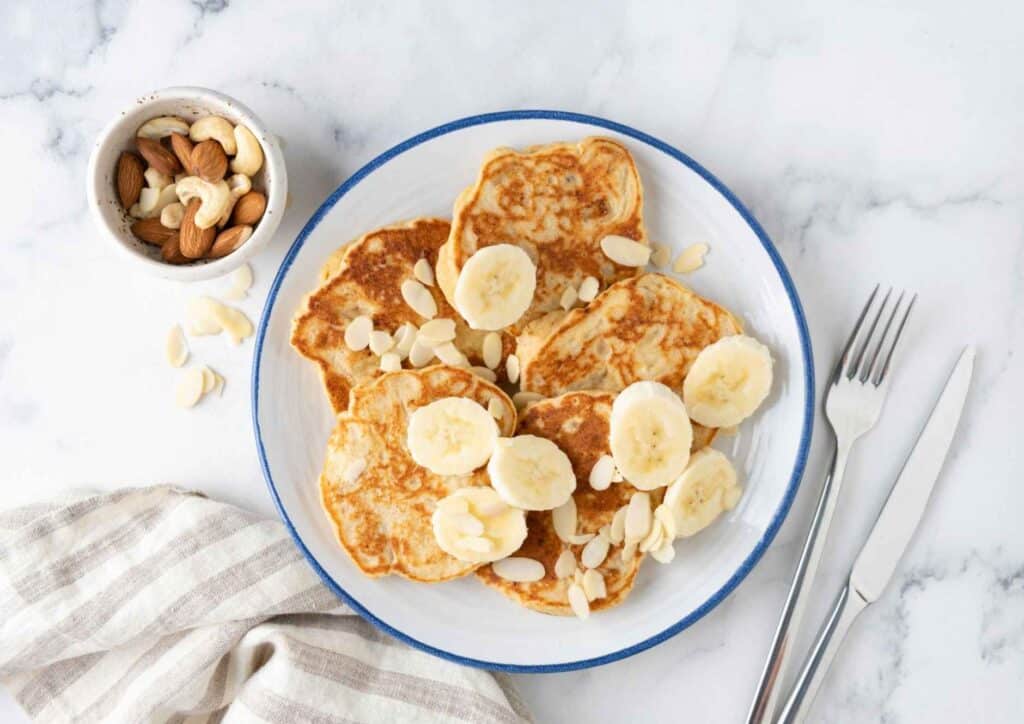 Protein Pancakes Breakfast Recipe for Weight Loss 1 A white plate holds stacked pancakes topped with sliced bananas and sprinkled almonds.