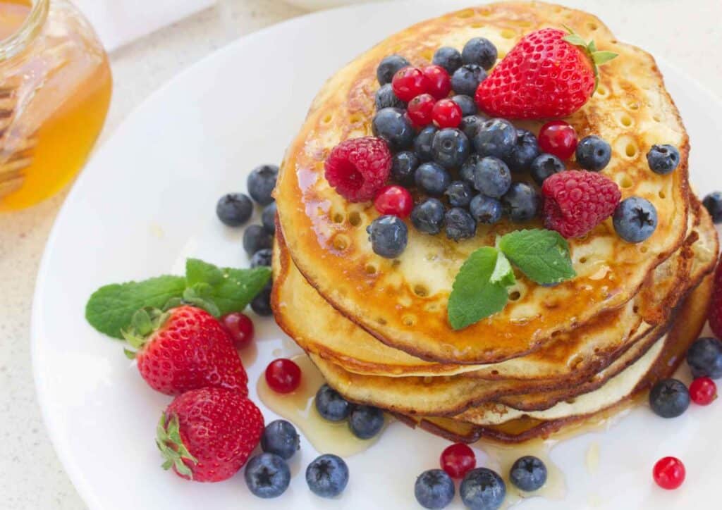 Protein Pancakes Breakfast Recipe for Weight Loss 3 A stack of fluffy pancakes topped with fresh berries and drizzled with honey, served on a white plate.