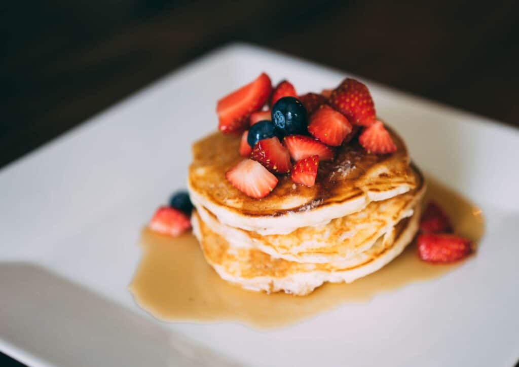 Protein Pancakes Breakfast Recipe for Weight Loss 8 A stack of golden pancakes topped with sliced bananas, served on a white plate.