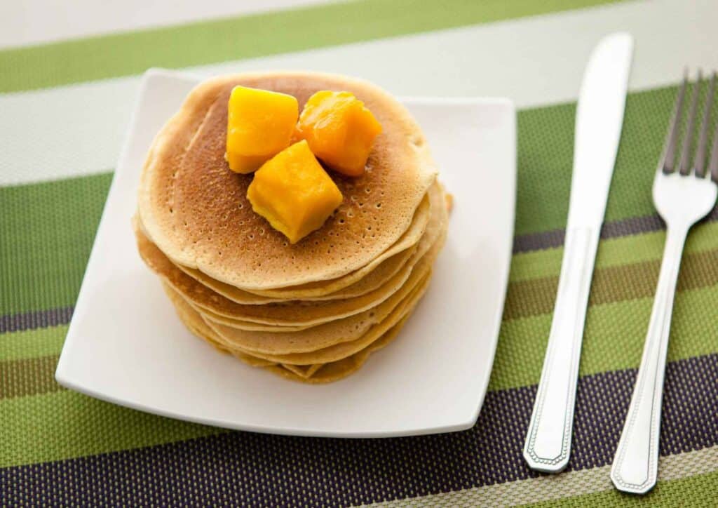 Protein Pancakes Breakfast Recipe for Weight Loss 4 A stack of golden pancakes topped with sliced bananas, served on a white plate.