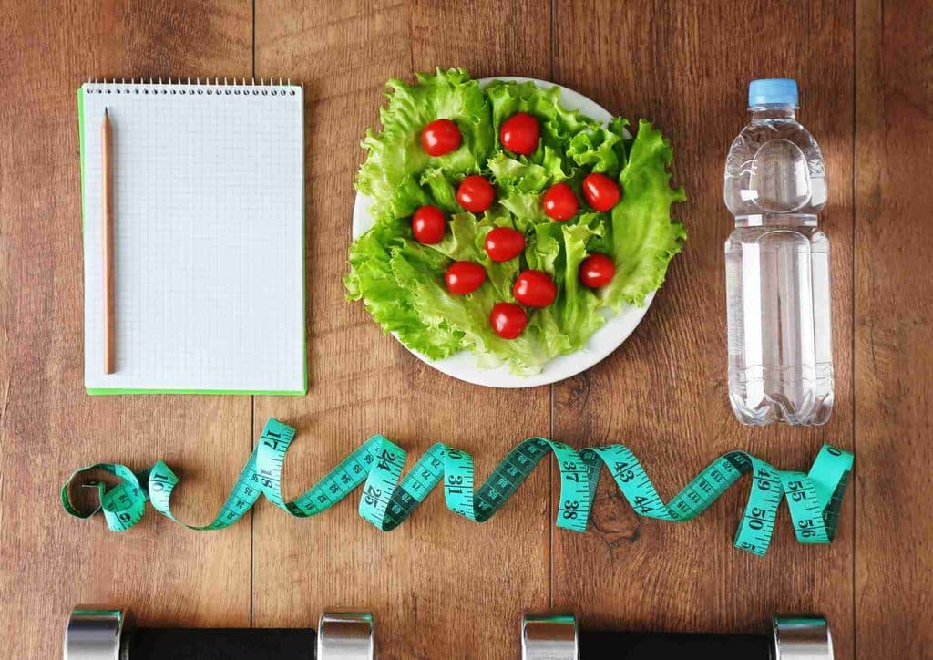 What Is a Sports Nutritionist? 7 A plate of assorted vegetables, a water bottle, a measuring tape, and a pair of dumbbells arranged on a table.