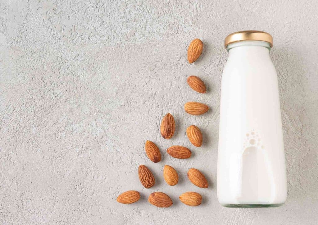 What Is a Sports Nutritionist? 9 Almond milk in a clear glass bottle, set against a smooth gray background.