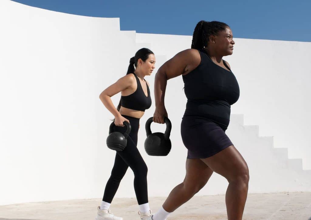 What Is Sustainable Weight Loss? 22 Two women in black sports attire walk while carrying kettlebells in a fitness setting.