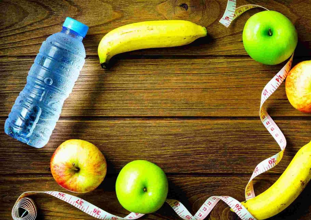 What Is Sustainable Weight Loss? 21 A bottle of water, red apples, yellow bananas, and a measuring tape arranged on a surface, symbolising health and fitness.