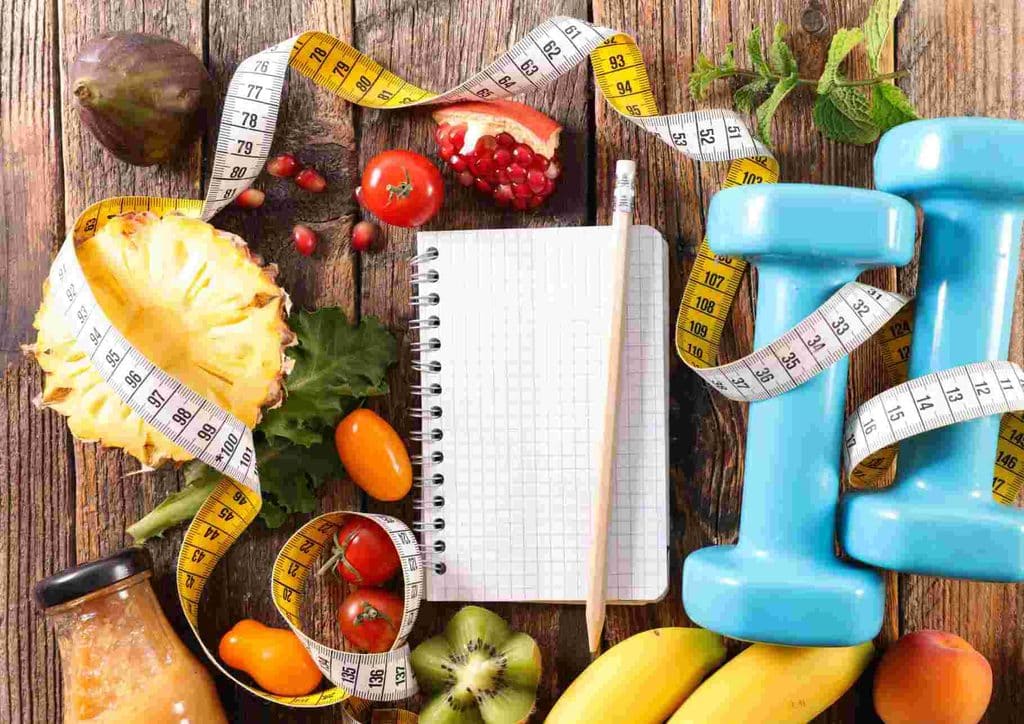 What Is Sustainable Weight Loss? 16 A notebook, measuring tape, and assorted fruits and vegetables arranged on a table, suggesting healthy lifestyle planning.