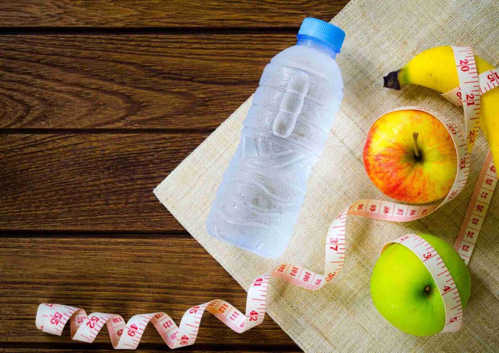 What Is Sustainable Weight Loss? 23 A bottle of water, red apples, yellow bananas, and a measuring tape arranged on a surface, symbolizing healthy living.