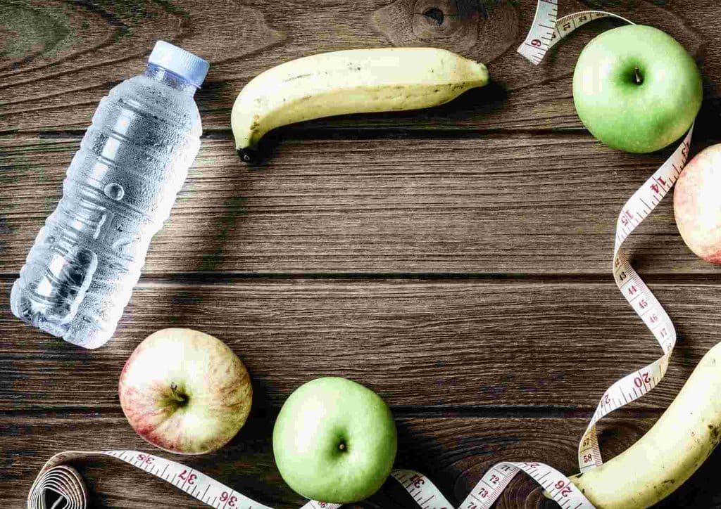 What Is Sustainable Weight Loss? 24 A bottle of water, red apples, yellow bananas, and a measuring tape arranged on a surface, symbolising healthy eating and fitness.