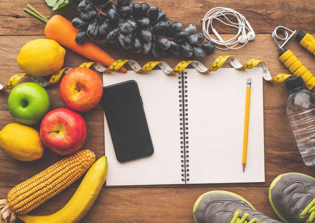 What Is Sustainable Weight Loss? 10 A notebook, sneakers, a water bottle, and assorted fruits and vegetables arranged on a flat surface.