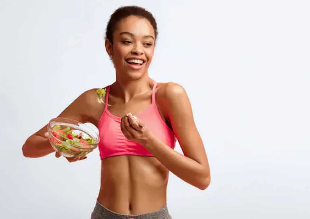 What Is a Sports Nutritionist? 15 A woman in a sports bra holds a bowl of fresh salad, promoting healthy eating and fitness.