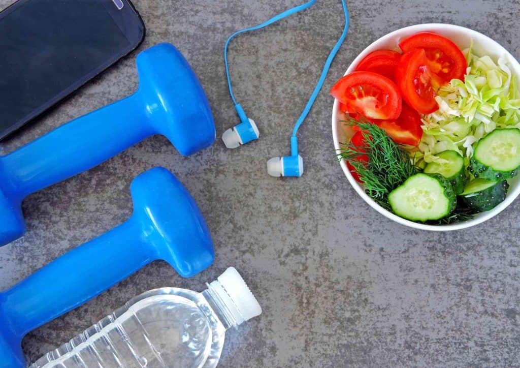 What Is a Sports Nutritionist? 8 A bowl of fresh vegetables, a pair of dumbbells, and headphones arranged on a table, promoting a healthy lifestyle.