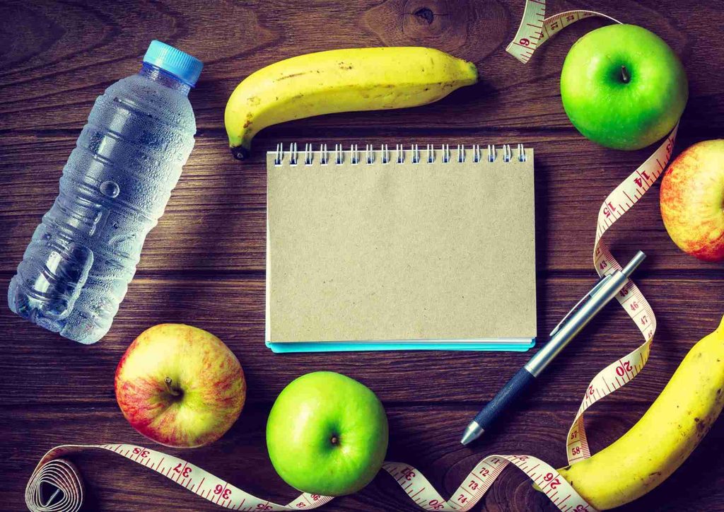 What Is Sustainable Weight Loss? 20 A notebook, water bottle, apples, and a measuring tape arranged on a wooden table, suggesting a healthy lifestyle theme.