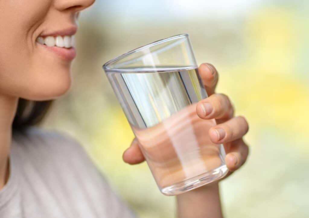 Is Coconut Water Good for Weight Loss? 9 A woman holding a clear glass of water, smiling while standing in a bright, well-lit room.
