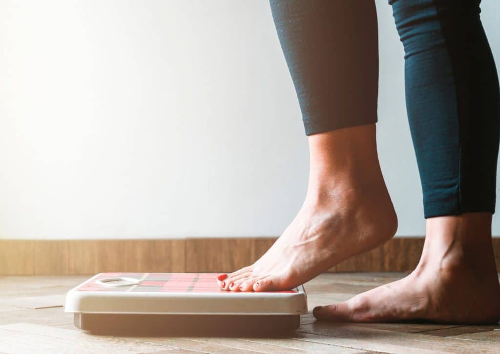 Not Losing Weight in a Calorie Deficit? Here's Why 14 A woman stands on a scale, looking down at the display with her feet positioned firmly on the device.