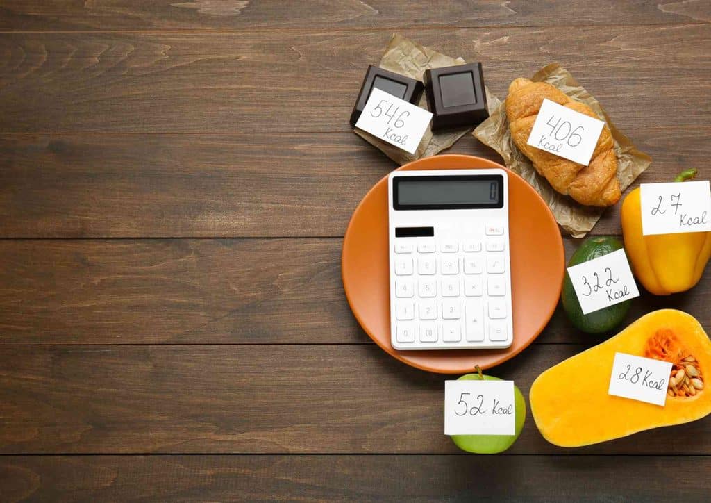 Not Losing Weight in a Calorie Deficit? Here's Why 15 A calculator next to a bag of bread, a banana, a pumpkin, and a bag of apples on a flat surface.