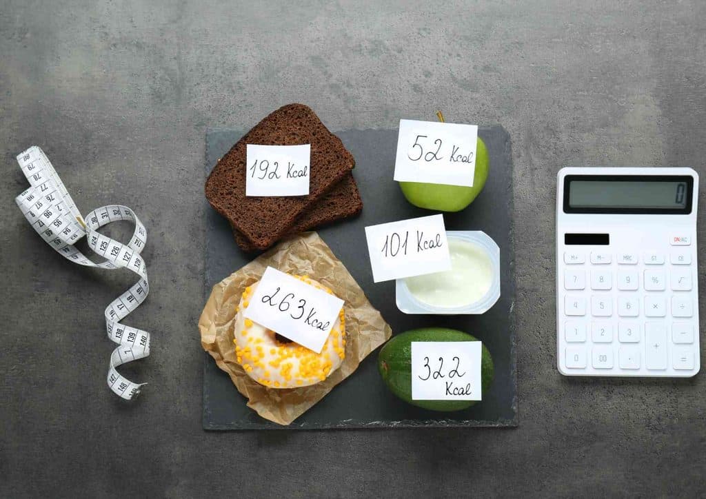 Not Losing Weight in a Calorie Deficit? Here's Why 10 A plate featuring a cup of coffee, a cup of tea, a banana, an apple, and a measuring tape arranged neatly.
