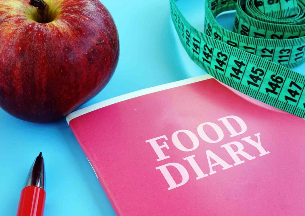 How to Lose Weight Without Exercise 27 A food diary displayed with a measuring tape and an apple, illustrating the concept of monitoring dietary habits.