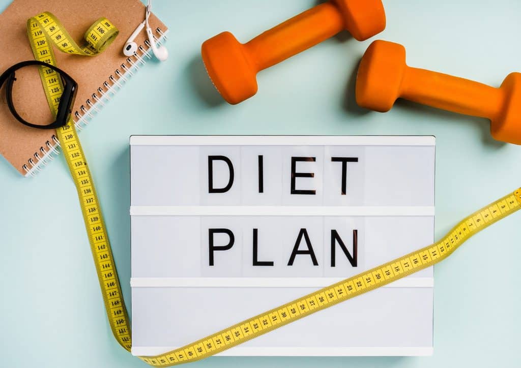 How to Lose Weight Fast (Safely, Without Crashing) 4 Dumbbells, a measuring tape, and a diet plan arranged on a blue background, symbolising fitness and health planning.