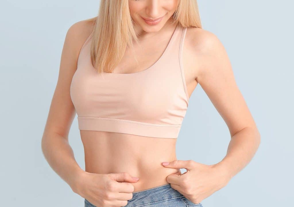How to Choose the Best Weight Loss Nutritionist in Sydney 7 A woman wearing a pink sports bra and jeans stands confidently, showcasing a casual athletic style.
