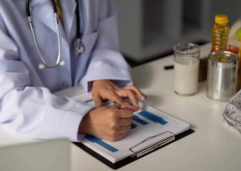 How to Choose the Best Weight Loss Nutritionist in Sydney 21 A doctor in a white coat writes notes on a clipboard, focused on patient information in a clinical setting.