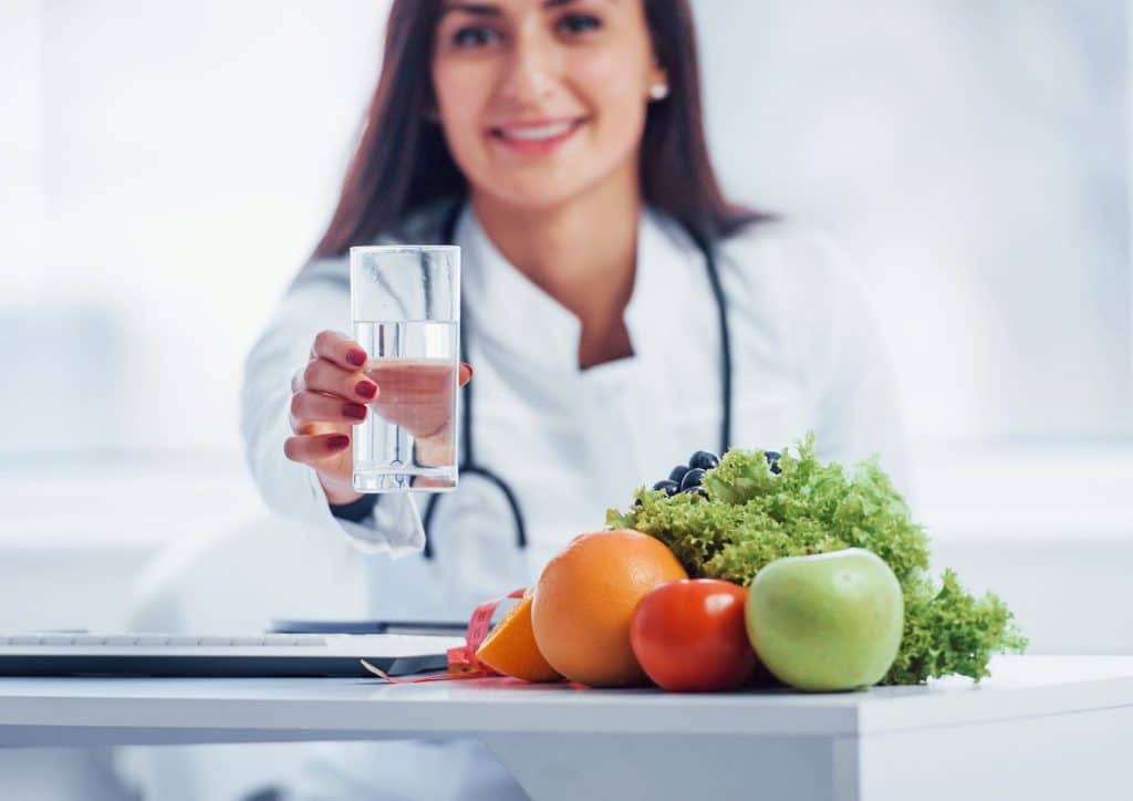 How to Choose the Best Weight Loss Nutritionist in Sydney 23 A woman in a white coat is holding a glass of water, smiling and looking towards the camera.
