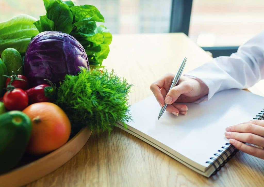 How to Choose the Best Weight Loss Nutritionist in Sydney 4 A person writes in a notebook with a pen, while a bowl of fresh vegetables sits nearby on the table.
