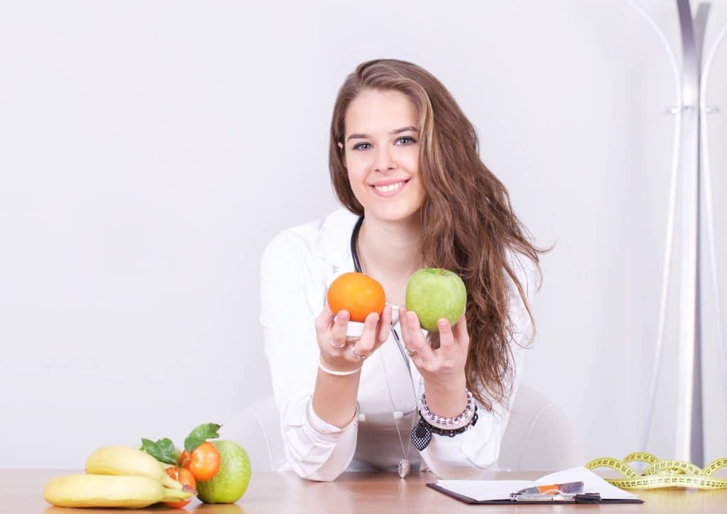 How to Choose the Best Weight Loss Nutritionist in Sydney 6 A woman holds an orange in one hand and an apple in the other, smiling at the camera.