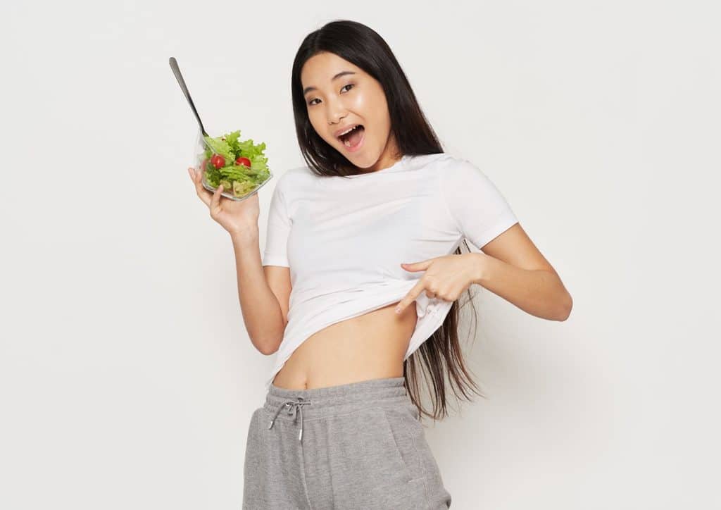How to Choose the Best Weight Loss Nutritionist in Sydney 8 Asian woman smiling while holding a fresh salad in her hand, showcasing vibrant vegetables and greens.