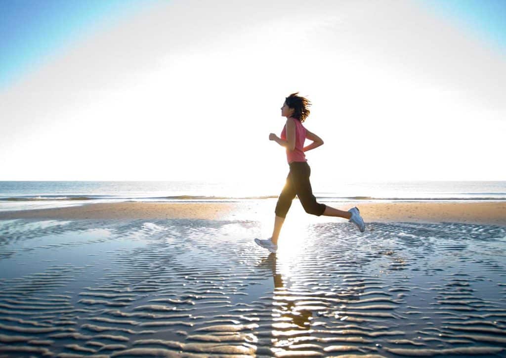 How to Lose Weight Fast (Safely, Without Crashing) 15 A woman runs along the beach during sunset, with vibrant orange and pink hues in the sky reflecting on the water.