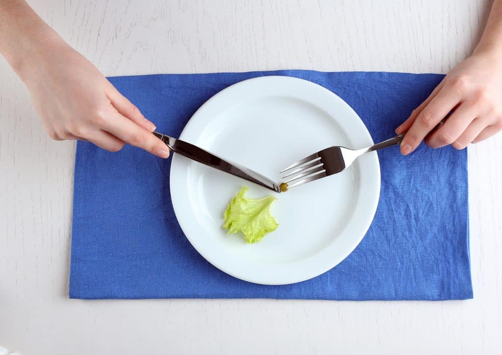 How to Lose Weight Fast (Safely, Without Crashing) 5 A person holds a fork and knife above a plate filled with fresh lettuce, preparing to eat.
