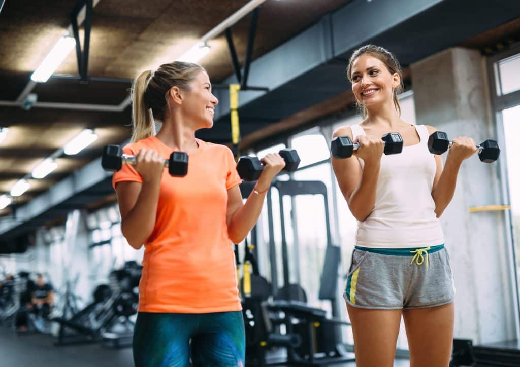 How to Lose Weight Fast (Safely, Without Crashing) 14 Two women in a gym, each holding a dumbbell, engaged in a strength training workout.