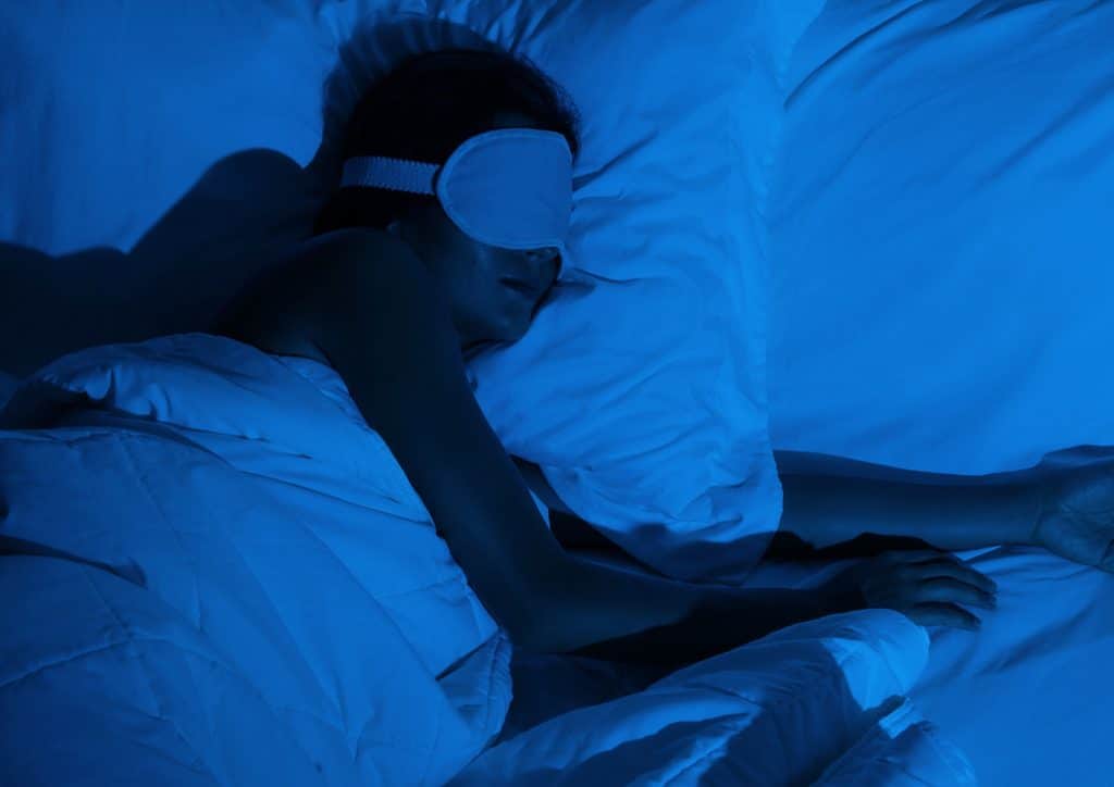 How to Lose Weight Fast (Safely, Without Crashing) 17 A woman peacefully sleeping in bed, wearing a blindfold to block out light.