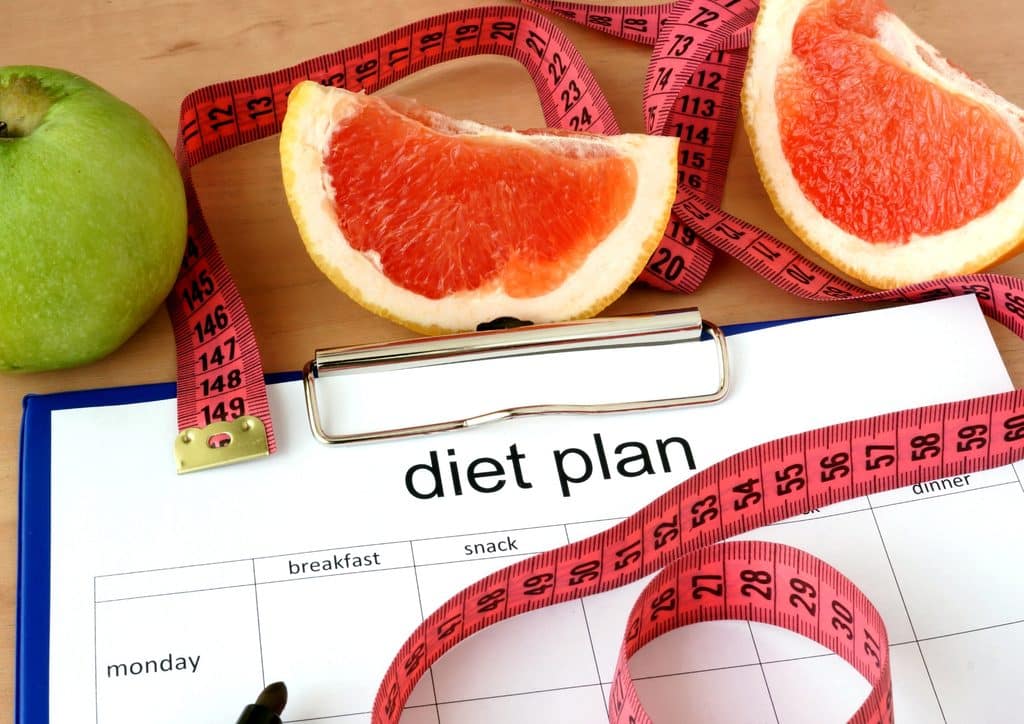 How to Lose Weight Fast (Safely, Without Crashing) 11 A diet plan on a table alongside a measuring tape, an apple, and a grapefruit, symbolising healthy eating choices.