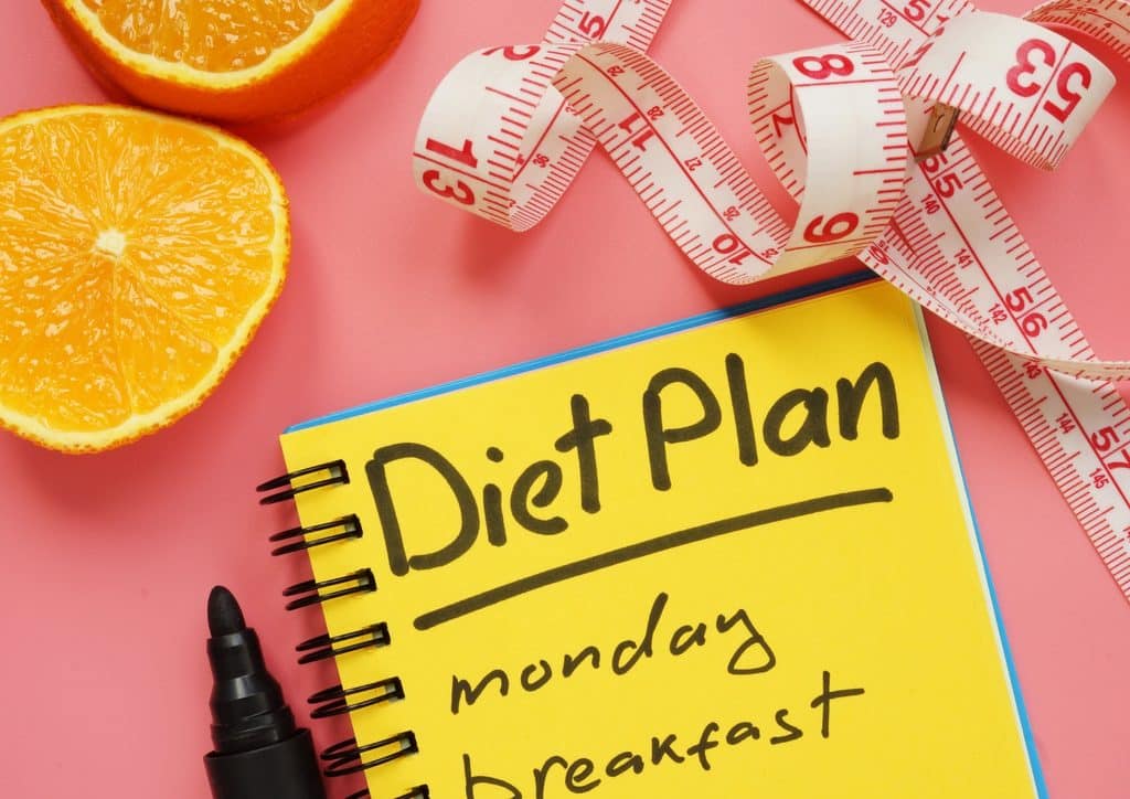 How to Lose Weight Fast (Safely, Without Crashing) 21 Diet plan on a notebook with a measuring tape and oranges, set against a pink background.