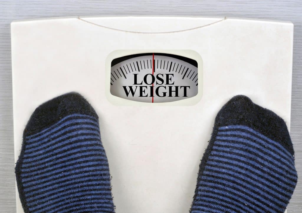 How to Lose Weight Fast (Safely, Without Crashing) 23 A person stands on a scale, with the phrase "lose weight" prominently displayed nearby.