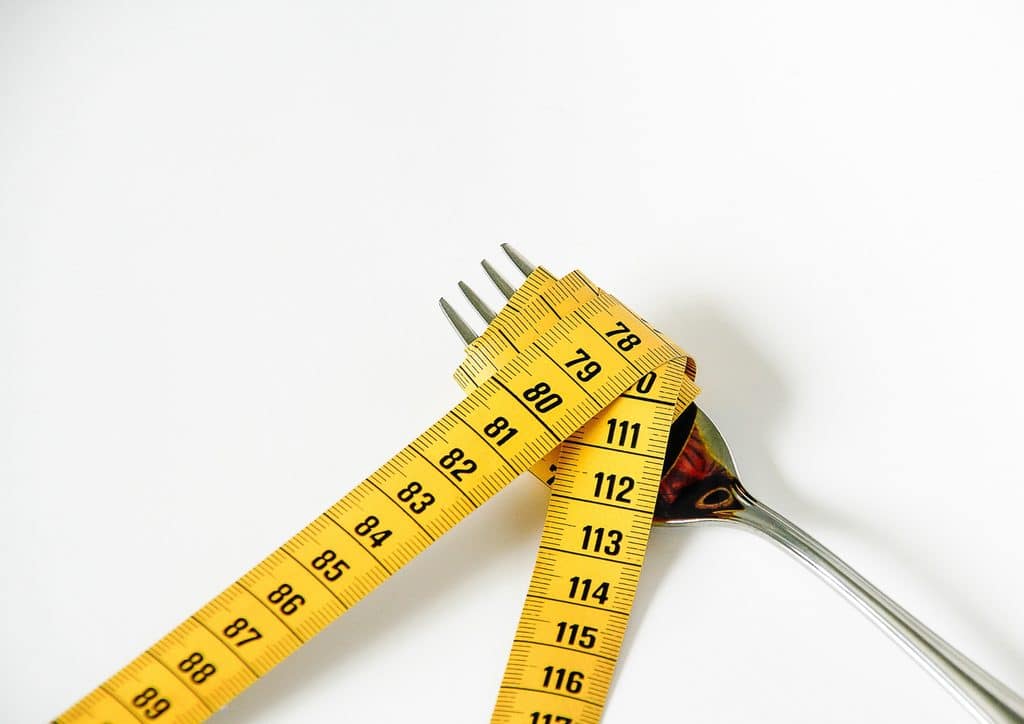 How to Lose Weight Fast (Safely, Without Crashing) 22 A measuring tape lies next to a silver fork, illustrating a comparison of size or measurement.