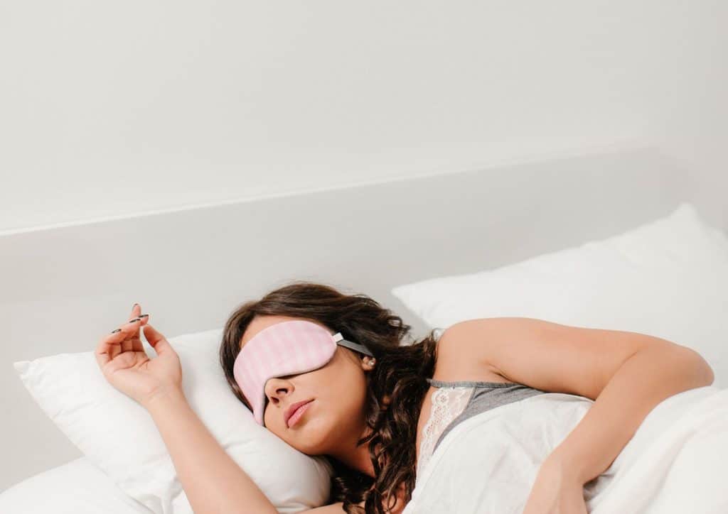 How to Lose Weight Fast (Safely, Without Crashing) 18 A woman peacefully sleeping while wearing a pink eye mask.