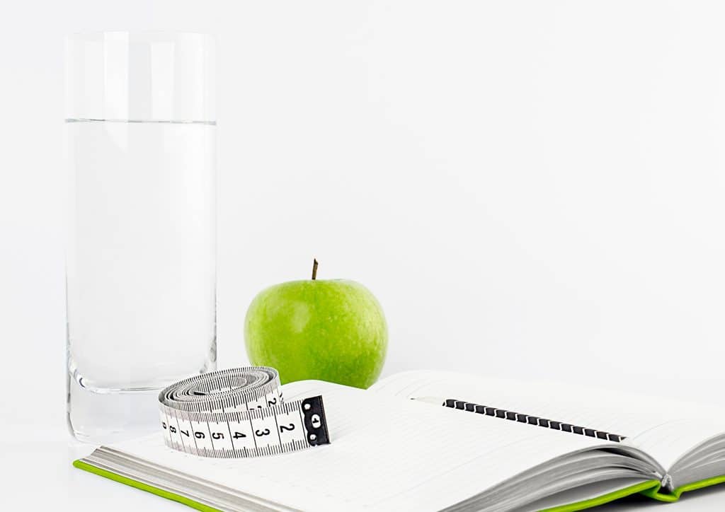 How to Lose Weight Fast (Safely, Without Crashing) 10 A notebook, a glass of water, and an apple arranged on a white background, symbolising study and healthy living.