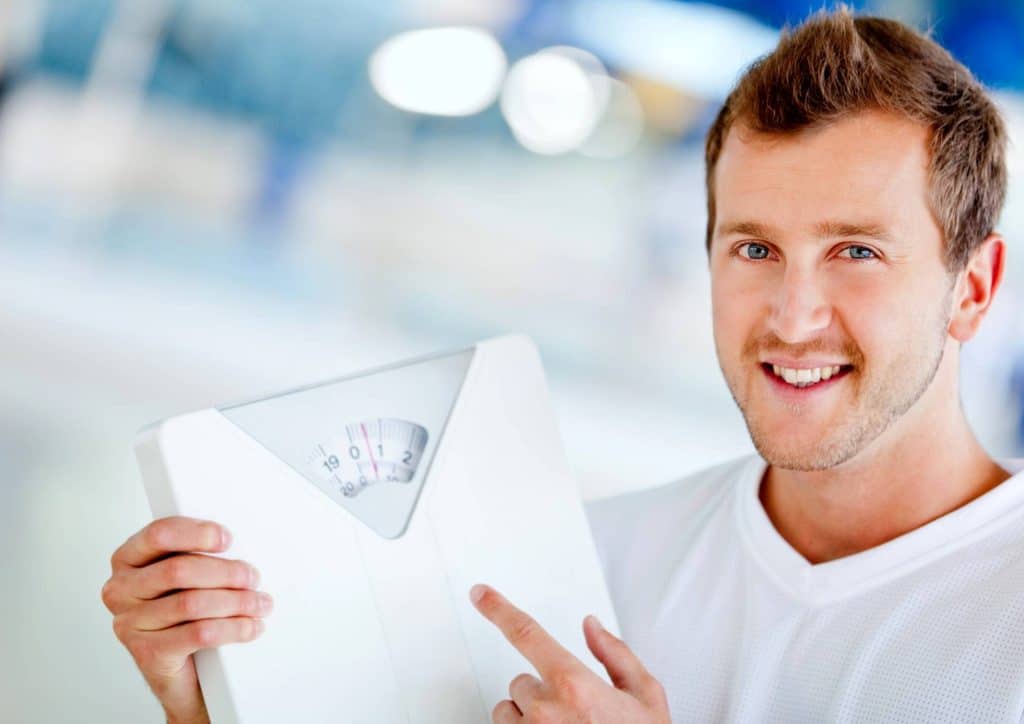 How to Lose Weight Without Exercise 19 A man stands holding a weight scale, looking focused and ready to measure weight.