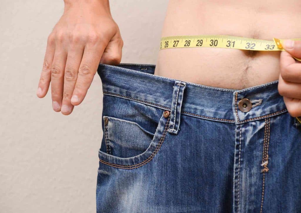 How to Lose Weight Without Exercise 5 A man measuring his waist with a tape measure, focusing on his midsection for accurate sizing.