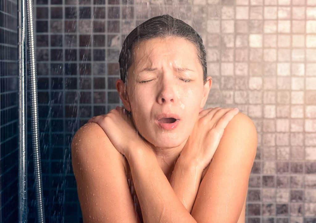 How to Speed Up Your Metabolism (What Actually Works) 5 A woman stands in the shower, hands on her face, conveying a moment of reflection or distress.