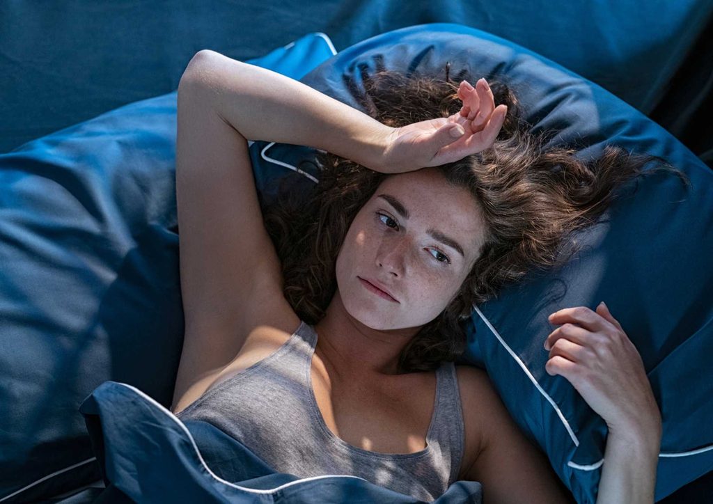 Why Am I Not Losing Weight? 8 Reasons a Nutritionist Sees Every Week 12 A woman resting in bed, her head comfortably positioned on a pillow, exuding a sense of relaxation and tranquility.