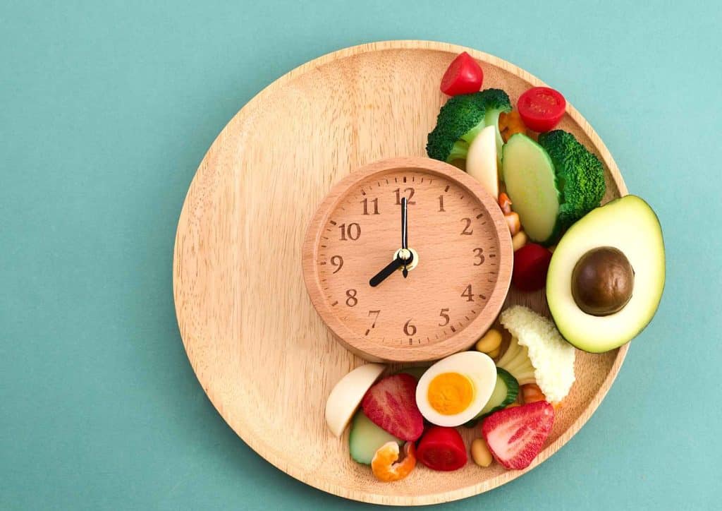 Intermittent Fasting for Weight Loss: Does It Actually Work? 4 A wooden plate featuring a clock at the centre, encircled by an assortment of colourful vegetables.