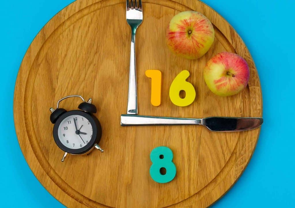 Intermittent Fasting for Weight Loss: Does It Actually Work? 21 A wooden clock, fork, knife, and apple arranged on a cutting board, showcasing a kitchen setting.