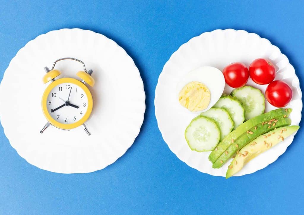 Intermittent Fasting for Weight Loss: Does It Actually Work? 8 Two plates of food are placed on a table next to an alarm clock, indicating mealtime and time management.
