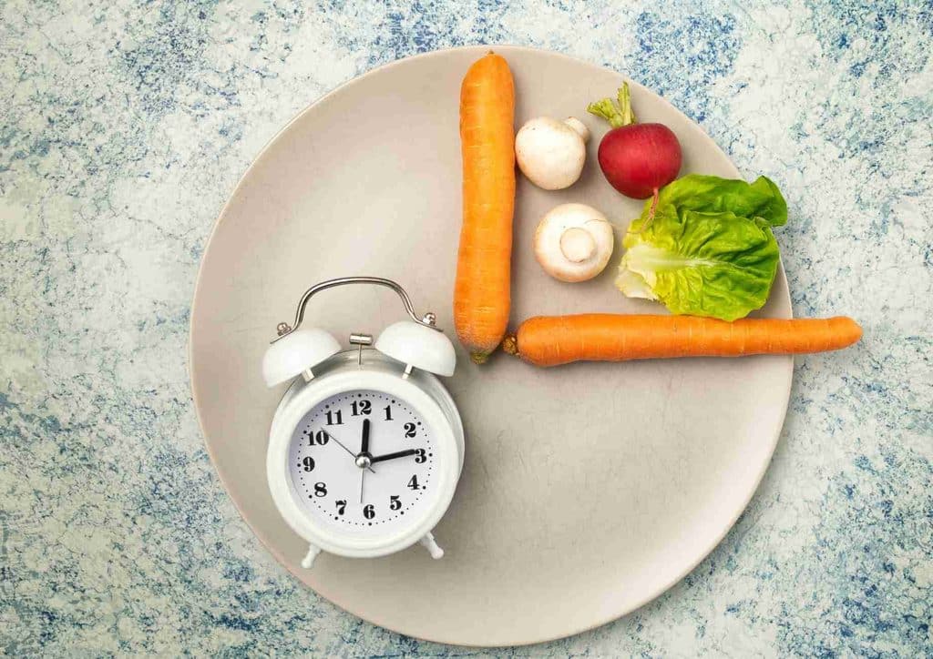 Intermittent Fasting for Weight Loss: Does It Actually Work? 10 A vibrant assortment of vegetables arranged on a plate beside an alarm clock, representing the importance of meal timing.