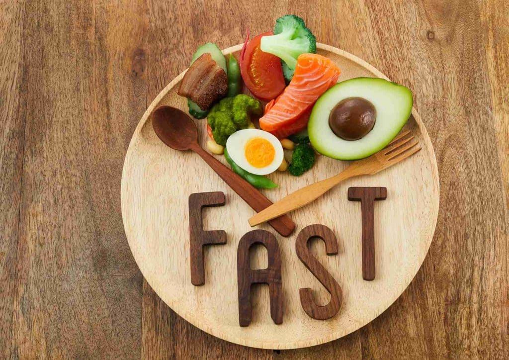 Intermittent Fasting for Weight Loss: Does It Actually Work? 17 A wooden plate holds various fast food items, with the word "FAST" displayed in wooden letters beside it.