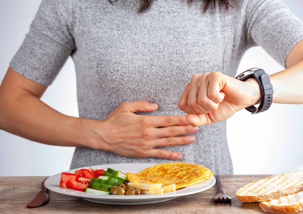 Intermittent Fasting for Weight Loss: Does It Actually Work? 7 A woman holds her stomach while enjoying a plate of food, indicating satisfaction or fullness.
