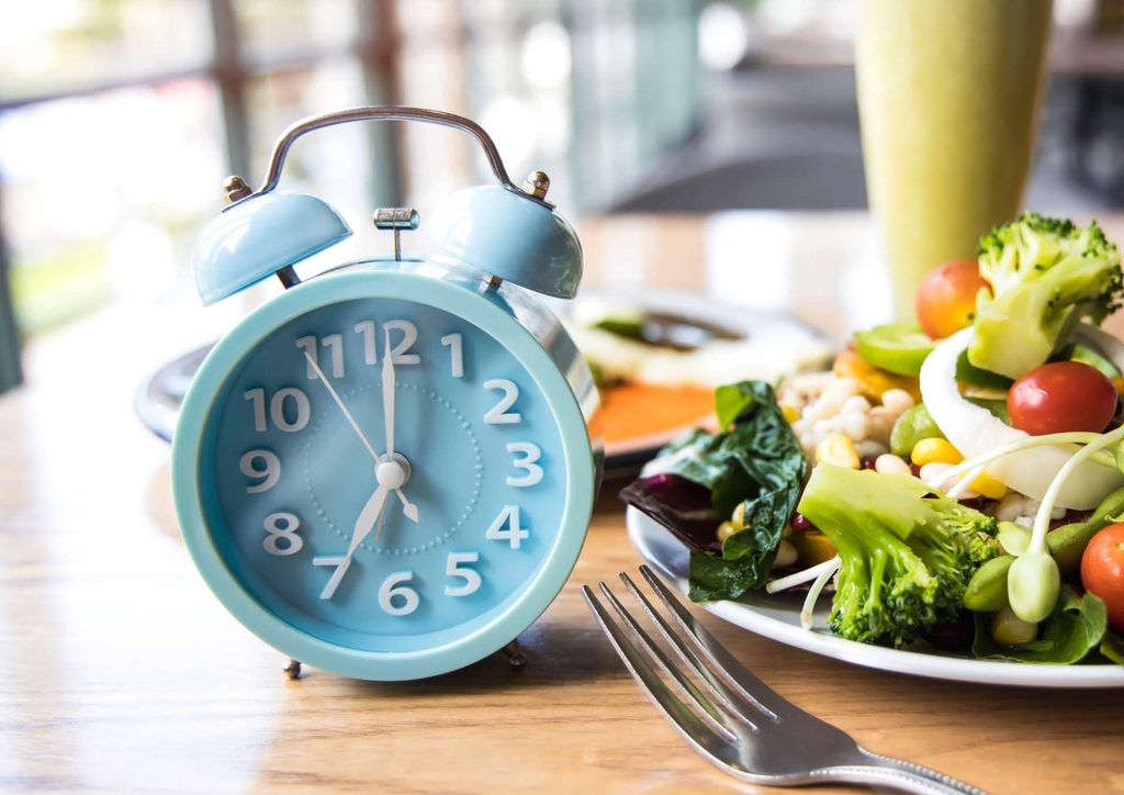 Intermittent Fasting for Weight Loss: Does It Actually Work? 11 A plate of food accompanied by a clock and a fork, indicating mealtime and the passage of time.